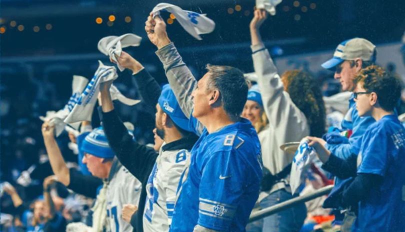 Fans in blue and white wave towels, cheer loudly in a stadium packed with energy and team spirit.